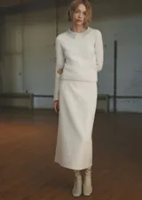 Falda midi de corte recto confeccionada en tejido bouclé color crudo. Presenta tiro medio, cintura elástica, cierre lateral y una abertura en la parte posterior.