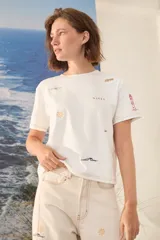 Remera blanca de algodón con bordados coloridos inspirados en la playa, de corte recto y manga corta.