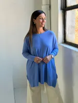 Sweater de punto color celeste, de corte holgado y diseño asimétrico con tajos laterales. Presenta cuello redondo, mangas largas y una costura vertical central en el frente.