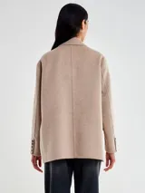 Chaqueta de paño color beige, de corte amplio y estructura clásica. Presenta solapas, cierre frontal con dos botones y bolsillos laterales con solapa.