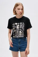 Remera de algodón negra con cuello redondo, manga corta y estampado frontal abstracto con detalles metalizados en tono plateado.