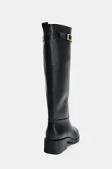 Bota de caña alta estilo hípica en color negro, con detalle de tira decorativa con hebilla metálica en la parte superior. Presenta tacón bajo ancho y punta redonda.