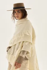 Ruana tejida en lana de cordero con diseño de sectores calados y terminación con flecos en los bordes.