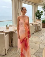 Vestido largo de satén con estampado degradado en tonos rosado, naranja y fucsia. Presenta escote en V, tirantes finos y un pañuelo integrado al cuello.
