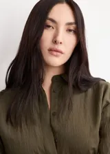 Vestido largo verde militar, con cuello camisero, cierre frontal con botones, mangas tres cuartos y diseño evasé. Incluye un cinturón fino de poliuretano con hebilla metálica.