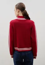 Campera tejida de punto color marrón con cierre frontal completo, cuello alto y detalles de rayas blancas en cuello, puños y ruedo. Presenta el logo de la marca estampado en el frente.