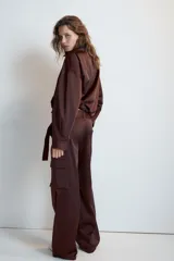 Pantalón cargo de tiro medio confeccionado en tejido satinado color beige, de corte recto y holgado. Cuenta con bolsillos laterales con solapa, bolsillos frontales y un cinturón integrado del mismo tejido con hebilla metálica.