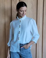 Camisa blanca de manga tres cuartos con cuello mao con volado y cierre frontal con botones marrones.