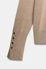 Jersey de punto liso en color beige, con cuello alto y manga larga con detalle de botones metálicos en los puños.