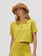 Chomba crop color beige, confeccionada en algodón, con cuello camisero que presenta rayas marrones y granates. Posee un pequeño logo bordado en el pecho.