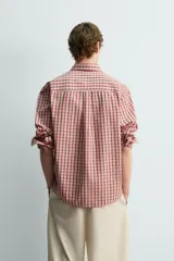 Camisa de algodón con cuello solapa, manga larga terminada en puño con botón y cierre frontal de botonadura. Presenta un patrón de cuadros en tonos rojo y beige.
