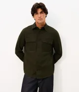 Camisa de manga larga confeccionada en sarga de algodón color verde militar. Presenta cuello inglés, cierre frontal con botones y dos bolsillos con solapa en el pecho.