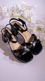 Sandalias negras de cuero sintético con tiras cruzadas en el empeine, pulsera con hebilla al tobillo y taco cuadrado.