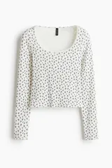Remera corta de punto acanalado color blanco con estampado floreado en negro, escote pronunciado con ribete de encaje y pequeño lazo al centro, y mangas largas.
