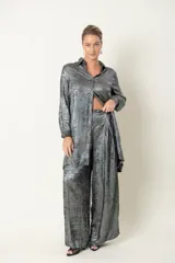 Camisa plateada de poliéster con textura metalizada, corte amplio, cuello clásico, cierre frontal con botones y mangas largas con puños abotonados.