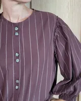 Camisa de manga larga con diseño de rayas verticales y bordados sutiles. Presenta cuello redondo, cierre frontal con botones y mangas abullonadas con volados en los hombros.