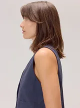 Chaleco negro sin mangas, de corte recto y largo a la cintura, con cuello redondo y cierre frontal oculto.