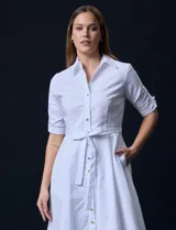 Vestido camisero blanco de algodón con cuello con solapa, delantera abotonada, mangas 3/4 regulables con presilla y botón, y cintura con lazo de ajuste.