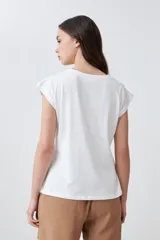 Blusa blanca de algodón con frente de tela broderie, cuello redondo y mangas cortas con diseño de hombros caídos.