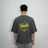 Remera gris de corte oversize con cuello redondo y mangas cortas. Estampado en la espalda con una estrella delineada en blanco, la palabra "Venefo" en amarillo y la frase "Pray to your father who is in the secret place" en letras blancas.
