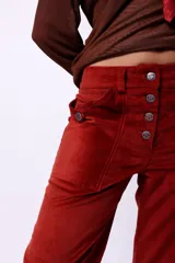 Pantalón de tiro alto confeccionado en pana color óxido. Presenta cierre frontal con botonadura metálica, bolsillos plaqué laterales y diseño de pierna flare.