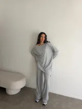 Conjunto gris melange compuesto por un buzo de cuello bote amplio y corte asimétrico con bolsillos, y un pantalón largo de corte recto y holgado.