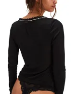 Remera de manga larga ajustada confeccionada en tejido de punto ligero tipo pointelle. Presenta escote en V con detalle de encaje y cintas entrelazadas decorativas.