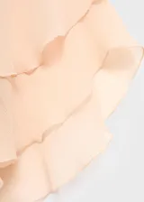 Blusa de viscosa color beige, con diseño de volantes frontales, cuello escotado con cierre de lazo y mangas largas acampanadas con volantes en los puños.