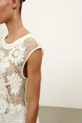 Top de crochet color crudo, sin mangas, con cuello redondo y detalle de aplicaciones de flores en relieve.