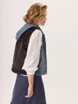 Chaleco con capucha, presenta una espalda de pelo sintético en color marrón oscuro con etiqueta de cuero negra y una capucha de tela tipo denim azul. Diseño original con mezcla de texturas.