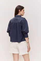 Camisa azul marino de cuello clásico, mangas abullonadas a tres cuartos y detalle fruncido en el frente. Presenta una silueta amplia y diseño corto con vuelo en el ruedo.