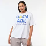 Remera blanca de corte oversize y manga corta, con estampa frontal en tonos azules y amarillos que incluye el texto 'Costa Azul' y 'Palma de Mallorca'.