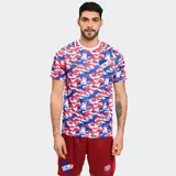 Remera deportiva Umbro de entrenamiento del Club Nacional de Football, con estampado de camuflaje en tonos rojo, blanco y azul. Presenta cuello redondo y el escudo del club en el pecho.