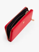 Billetera rectangular color rojo, con cierre perimetral de cremallera y herrajes dorados. Presenta una insignia metálica con el monograma TH en el frente.