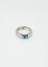 Anillo de acero quirúrgico color plateado con una zirconia azul ovalada engarzada.