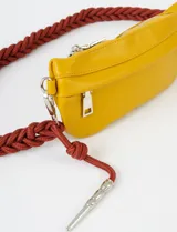 Riñonera amarilla de cuero sintético con asa trenzada marrón y cierre superior con cremallera.