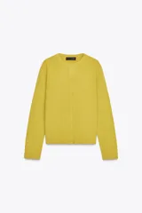 Chaqueta de punto color amarillo mostaza, con cuello redondo, manga larga y cierre frontal con botones. Los acabados son en rib a tono.