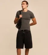 Bermuda baggy de jean color negro con pespuntes contrastantes, cierre de botón y cremallera, y bolsillos.