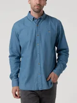 Camisa de manga larga color azul claro, confeccionada en tela tipo denim o chambray, con cuello abotonado (button-down) y un pequeño logo bordado de un pato en el pecho.