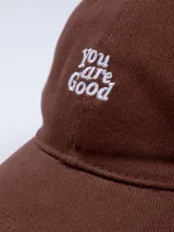 Gorro marrón de gabardina con visera y bordado frontal con la frase "You are Good" en color blanco.