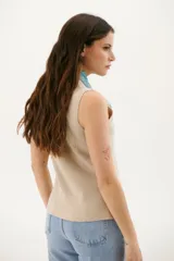 Chaleco tejido de punto en color beige, con escote en V, cierre frontal con botones oscuros y bolsillos frontales decorativos.