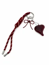 Llavero de cuerda bordó con detalles blancos, que incluye un dije de corazón de resina, un dije de lazo metálico y herrajes plateados.