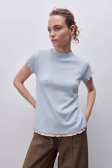 Remera celeste de calce semi ajustado, confeccionada en tejido acanalado con cuello alto, mangas cortas raglán y terminaciones onduladas en cuello, mangas y ruedo.