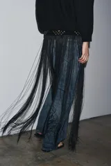 Cinturón tipo fajín negro de 10 cm de ancho, confeccionado en piel 100%. Presenta una sección superior con tachas doradas y ojales metálicos, y la parte inferior terminada en flecos largos. Se ajusta al frente con una lazada de cordón negro.