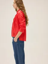 Camisa de lino color crudo, con cuello mao y cierre frontal con botones. Cuenta con detalles de alforzas verticales y diseño bordado floral en el frente, además de mangas 3/4 con volumen y puños elásticos.