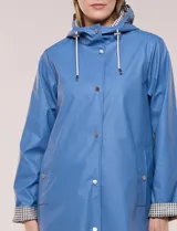 Pilot engomado impermeable color azul, de corte recto estilo trench con acabado resistente al agua. Cuenta con capucha integrada, cierre frontal con broches a presión, bolsillos laterales con ojal y forro interior de tela estampada a cuadros visible en la solapa y los puños.