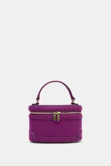 Bolso tipo vanity de estructura rígida en color fucsia, con acabado aterciopelado. Presenta un asa de mano superior, cierre de cremallera metálica dorada con doble tirador y correa bandolera ajustable y extraíble.