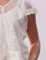 Blusa de dos piezas color blanco, marca Cupio. La pieza superior es de tul bordado con escote en V con botones, manga corta amplia y ruedo con puntilla bordada. Incluye forro interno a tono.