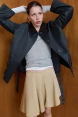 Chaqueta encerada de corte recto con cuello de solapa en pana marrón. Presenta manga larga, bolsillos delanteros de vivo y de plastrón con solapa, y un cinturón de lazada en el mismo tejido. Incluye cierre frontal con botones ocultos por tapeta y abertura en la espalda.