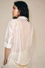 Camisa blanca de tejido semitransparente ZARA Woman Collection, con cuello redondo, manga corta y detalle de pañuelo integrado en el mismo tejido al cuello. Cierre frontal con botones.